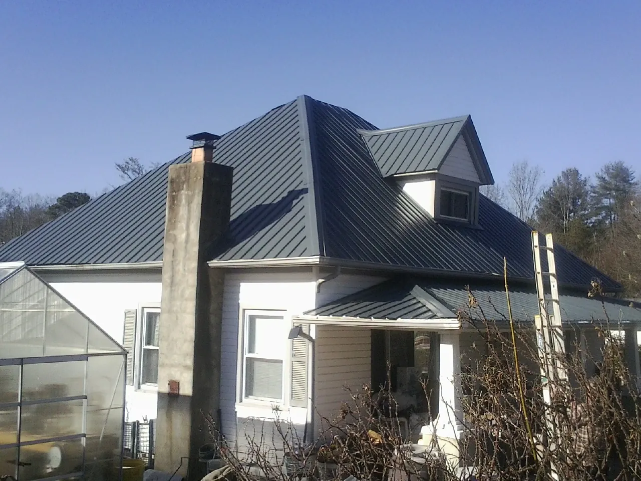 Dark blue standing seam metal roof on a white farmhouse with dormer — Slate & Tile Roof Repair by Roofing Brothers in Richville