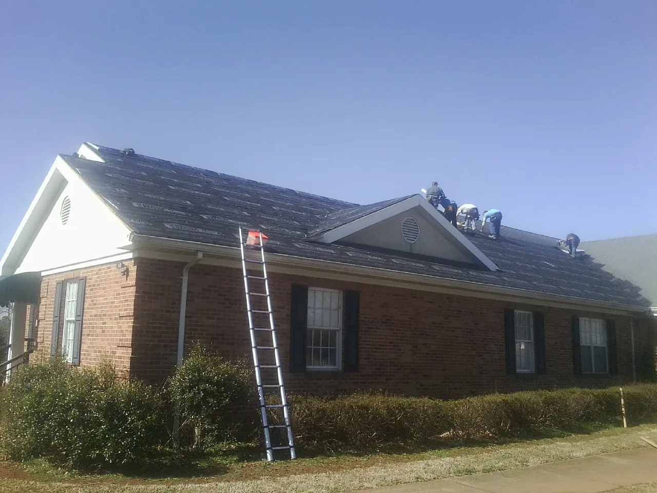 Crew tearing shingles off a brick ranch roof with a ladder set — Emergency Roof Repair work by our crew in Richville
