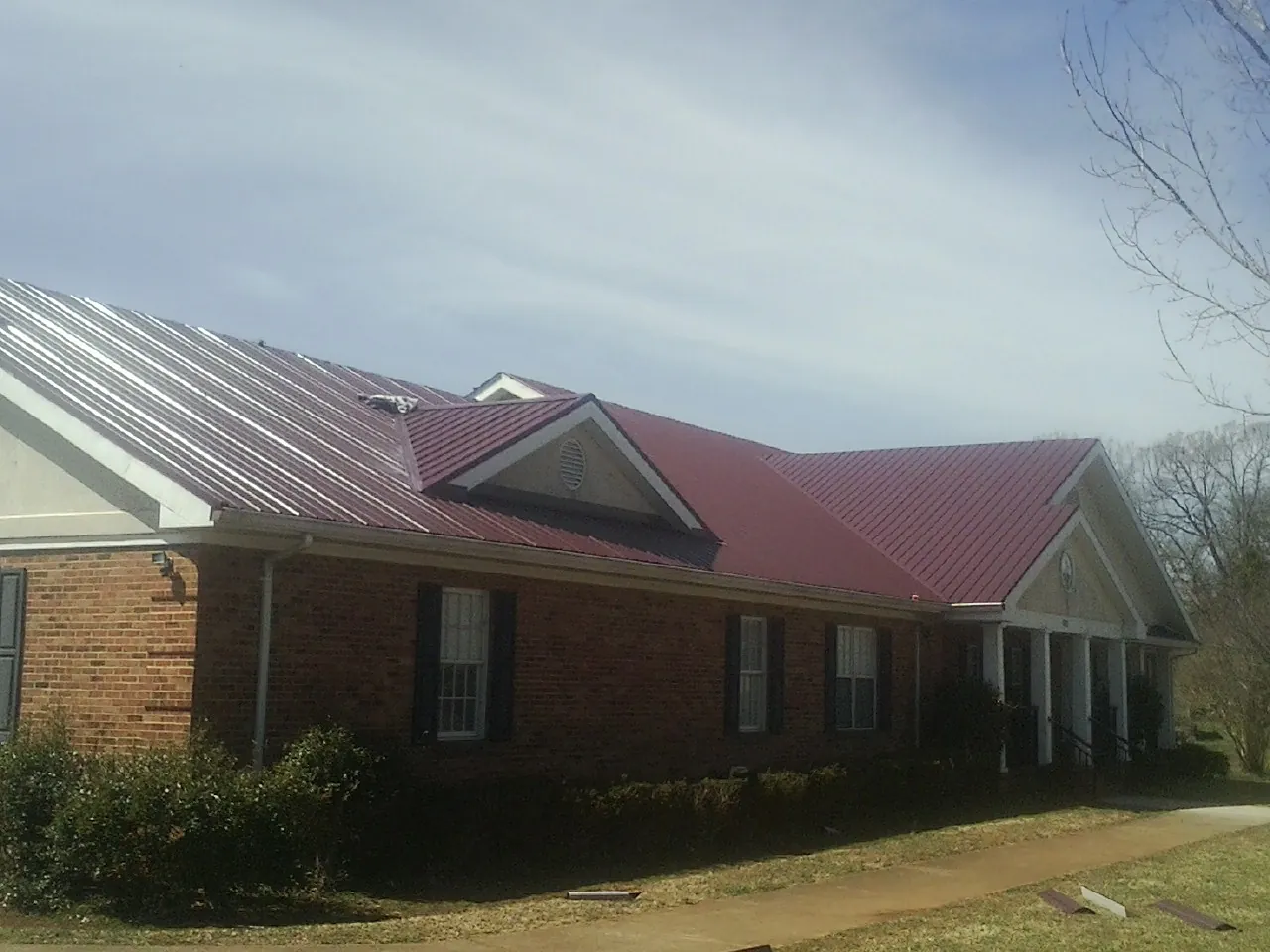 Red metal roof with gabled entries on a long brick building, from a Hail Damage Roof Repair job in Richville