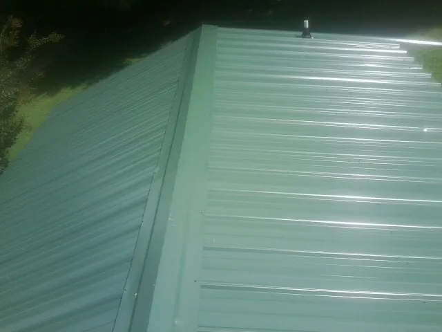 New green metal panels meeting at the ridge of a roof — Flat Roof Repair work by our crew in Richville