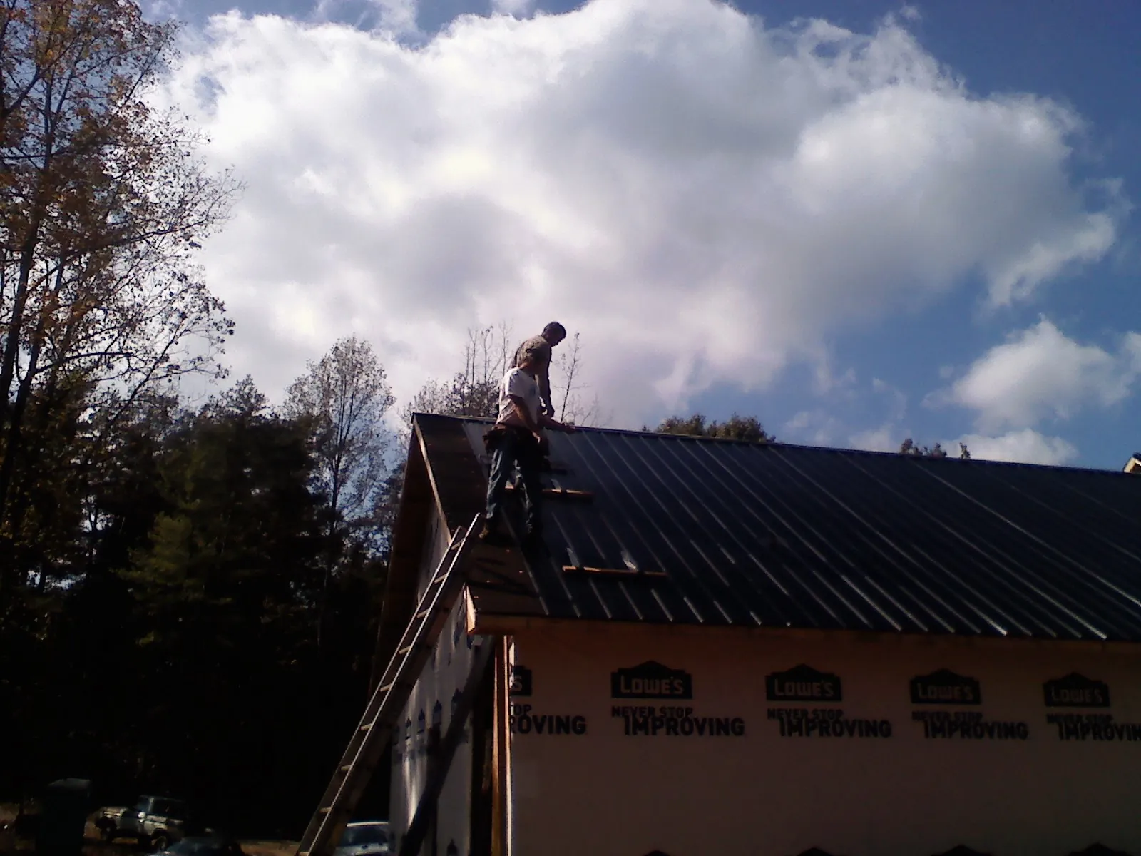 Roofer fastening dark metal panels high against a cloudy sky, from a Roof Inspection job in Richville