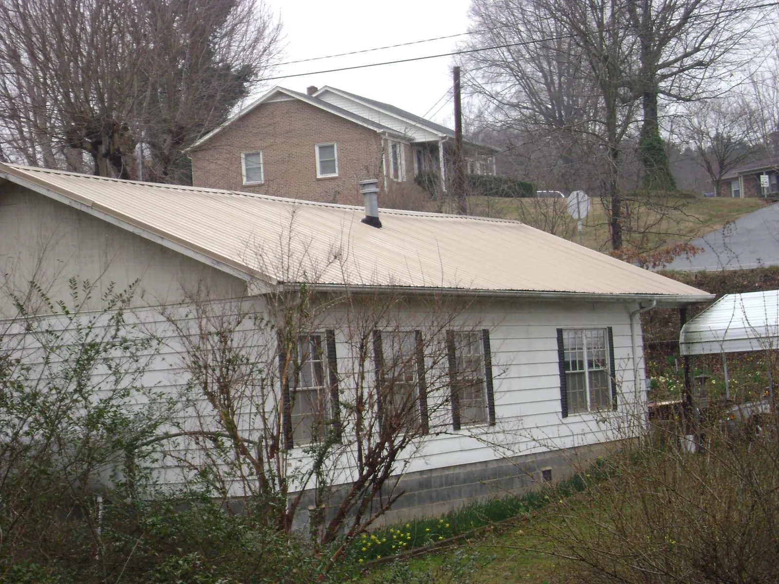 Tan metal roof on a white sided house set into a hillside — Commercial Roofing by Roofing Brothers in Richville